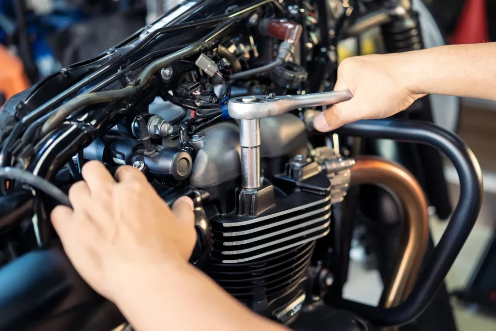 Meccanico che monta un pezzo di ricambio della moto con una chiave inglese e una presa